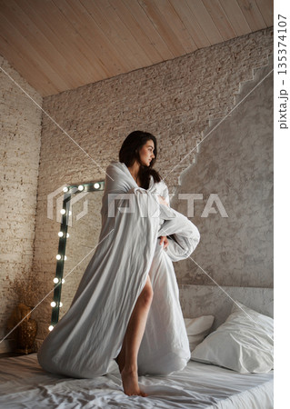 A woman with black hair wakes up in the morning in a white blanket and catches the rays of the sun. The portrait is creative, with brown eyes. High quality photo A woman with black hair wakes up in the morning in a white blanket and catches the rays of the sun. The portrait is creative, with brown eyes. High quality photo 135374107