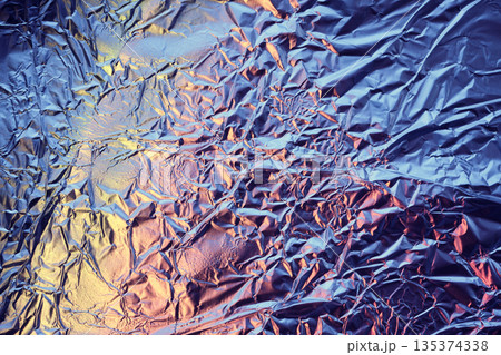 Crumpled aluminum foil surface reflecting vibrant blue and orange light 135374338
