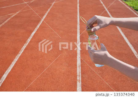 Athlete's hands prepare bottle of water for refreshment on red running track 135374340
