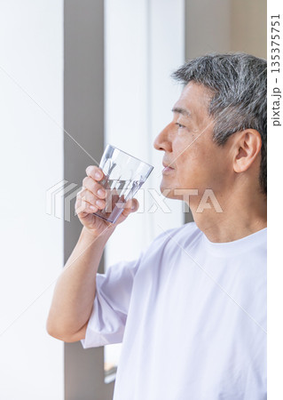 窓辺で水を飲むシニア男性 135375751
