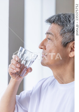 窓辺で水を飲むシニア男性 135375752