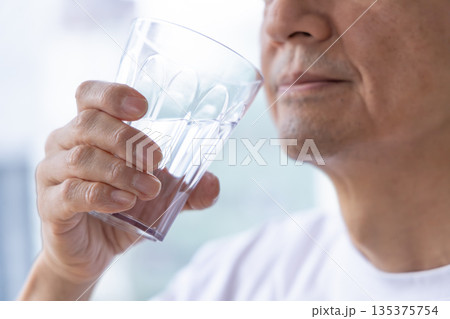 窓辺で水を飲むシニア男性 135375754