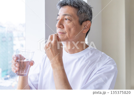 窓辺で薬を飲むシニア男性 135375820