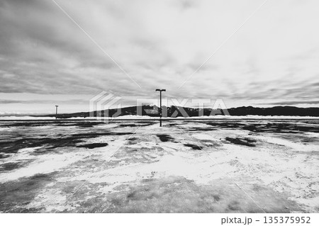 雪に覆われた駐車場と遠くに連なる山脈を背景にした冬の寒冷地のモノクロ風景 135375952