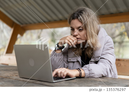 Woman working laptop concentrating on remote business outdoors at wooden table Woman working laptop concentrating on remote business outdoors at wooden table 135376297