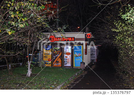 Small tobacco kiosk lit up at night on a fark path. Small kiosk on a dark path in a wooded area, lit up at night. Small tobacco kiosk lit up at night on a fark path. Small kiosk on a dark path in a wooded area, lit up at night. 135376797