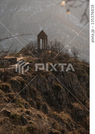 Stone watchtower of Harsnadzor standing on rocky hill in winter, framed by bare tree branches with soft bokeh, dramatic mountain gorge in background Stone watchtower of Harsnadzor standing on rocky hill in winter, framed by bare tree branches with soft bokeh, dramatic mountain gorge in background 135376816