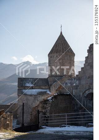 Stone drum and conical dome of the Cathedral of Saints Paul and Peter at the Tatev Monastery rise above snow-dusted roofs, mountain ridges Stone drum and conical dome of the Cathedral of Saints Paul and Peter at the Tatev Monastery rise above snow-dusted roofs, mountain ridges 135376924
