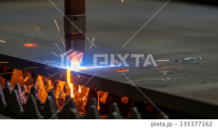 Plasma arc machine works on metal piece, creating sparks as it pierces through. Molten metal droplets separate and fall away from the area being cut. 135377162