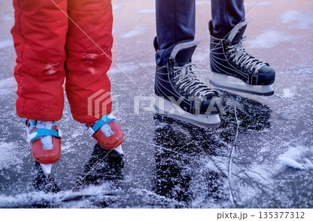 Skating shoes of a child and father in close-up standing on the ice of a frozen lake in the snow Skating shoes of a child and father in close-up standing on the ice of a frozen lake in the snow 135377312