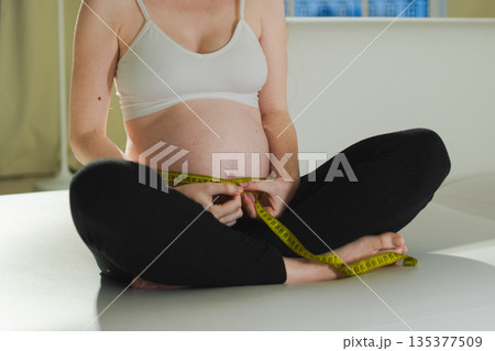 Pregnancy motherhood. Pregnant woman measuring big belly. Girl measuring her belly with tape to keep track of her fetus development. Woman enjoying pregnancy. Maternity tenderness parenthood new life 135377509