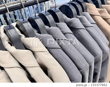 New stylish classic cut jackets in pastel shades are hanging on hangers in a clothing store. High quality photo 135377662