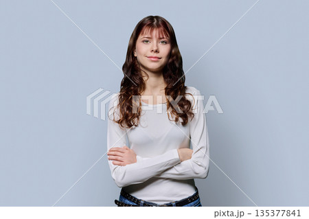 Portrait of smiling confident teenage girl with crossed arms on light background 135377841