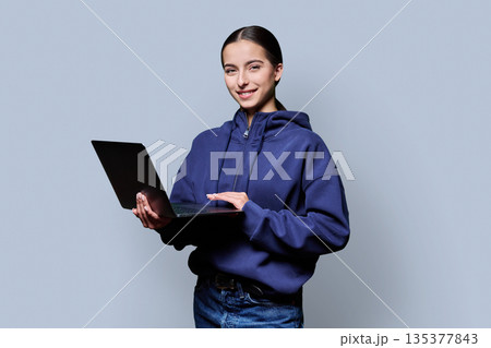 Portrait of smiling teenage girl holding laptop on gray studio background Portrait of smiling teenage girl holding laptop on gray studio background 135377843