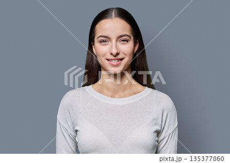 Portrait of beautiful smiling teenage woman against gray studio background Portrait of beautiful smiling teenage woman against gray studio background 135377860