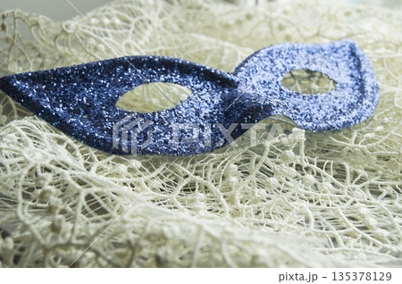 Brilliant blue carnival mask lies on beautiful lace. Fashion background Brilliant blue carnival mask lies on beautiful lace. Fashion background 135378129