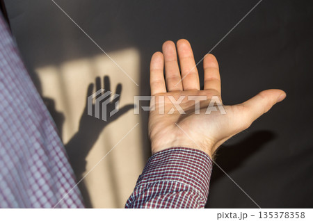The young man holds an empty hand with his palm up, a shadow on the wall The young man holds an empty hand with his palm up, a shadow on the wall 135378358