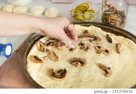 step-by-step pizza preparation, step 5, Female hands spread out the mushrooms on the pizza, homemade meal 135378410