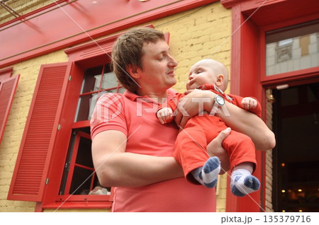 Father Holding Baby in Matching Red Outfits Outdoors 135379716