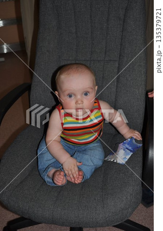 Cute Baby Sitting on a Chair Holding a Paper 135379721