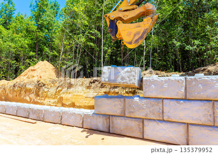Heavy machinery lifts places concrete blocks on construction site surrounded by retaining wall Heavy machinery lifts places concrete blocks on construction site surrounded by retaining wall 135379952