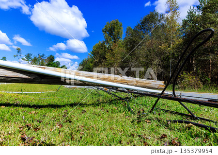 Utility pole lies on ground, surrounded by green grass trees, under hurricane storm Utility pole lies on ground, surrounded by green grass trees, under hurricane storm 135379954