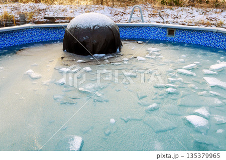 Swimming pool water is frozen with ice chunks floating black cover in center cold winter day. Swimming pool water is frozen with ice chunks floating black cover in center cold winter day. 135379965