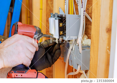 Electric worker uses drill to install circuit breaker in home repair work. Electric worker uses drill to install circuit breaker in home repair work. 135380004