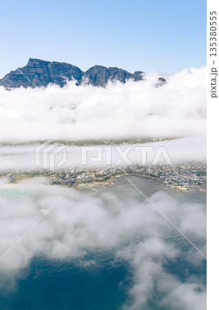 Aerial view of mountain peaks emerging from clouds above coastal city and ocean 135380555