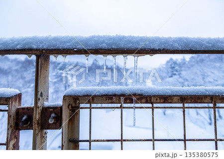 雪とつららが付いた錆びた金属フェンスの冬景色 135380575