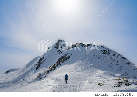 逆光の雪稜を歩く登山者と冬の稜線 逆光の雪稜を歩く登山者と冬の稜線 135380590