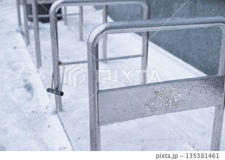 Empty metal bicycle parking rack covered in light snow and ice during winter in an urban setting. 135381461