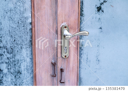 Close-up of a metal handle on a wooden door with frosted glass and ice, capturing the cold winter atmosphere Close-up of a metal handle on a wooden door with frosted glass and ice, capturing the cold winter atmosphere 135381470