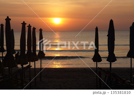 beach umbrellas and beach chair are arranged in an orderly manner, In the evening, the sun is about to set on the horizon background beach umbrellas and beach chair are arranged in an orderly manner, In the evening, the sun is about to set on the horizon background 135381810