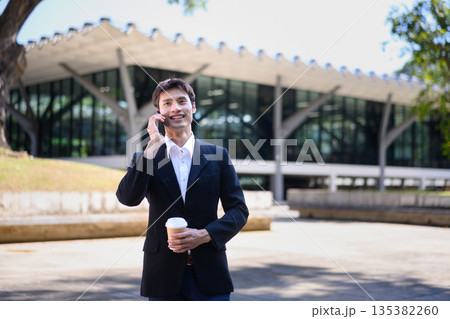 A man from an office walks outdoors talking on his phone while holding a coffee cup 135382260