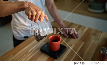 Closeup man pouring fresh drip coffee into a cup in a warm morning kitchen Closeup man pouring fresh drip coffee into a cup in a warm morning kitchen 135382338