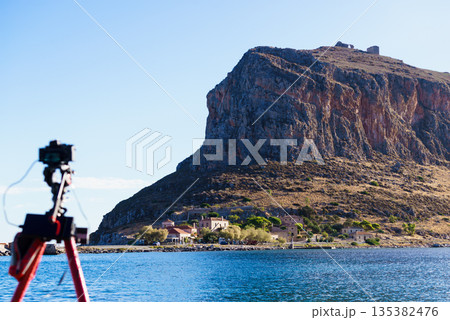 Camera on tripod and Monemvasia island Camera on tripod and Monemvasia island 135382476