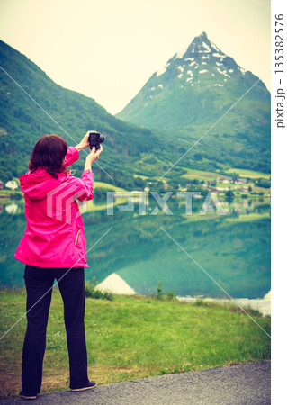 Tourist taking photo at norwegian fjord lake Tourist taking photo at norwegian fjord lake 135382576