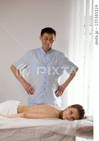 Portrait of a doctor massagist and patient - young woman lying on massage table - before SPA procedure Portrait of a doctor massagist and patient - young woman lying on massage table - before SPA procedure 135383324