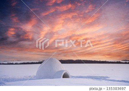 Snow igloo in the snowy field during incredible orange sunset 135383697