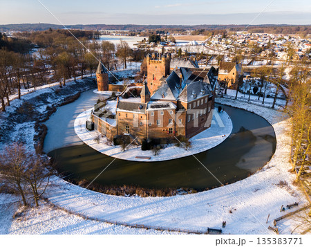 Sunlit red brick castle with conical towers and frozen moat anchors a snowy village, blending medieval elegance with winter serenity. Sunlit red brick castle with conical towers and frozen moat anchors a snowy village, blending medieval elegance with winter serenity. 135383771