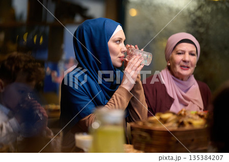 Muslim family enjoys iftar together in a restaurant with Ramadan decorations and warm lighting Muslim family enjoys iftar together in a restaurant with Ramadan decorations and warm lighting 135384207