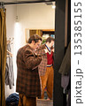 Elegant man trying on wool vintage blazer in fitting room, wearing clothing in front of mirror. 135385155