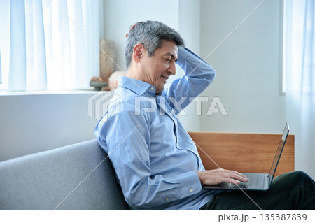 ソファに座ってノートパソコンを操作する60代男性 135387839