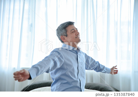 ベッドに座って伸びをするシニア男性 135387840