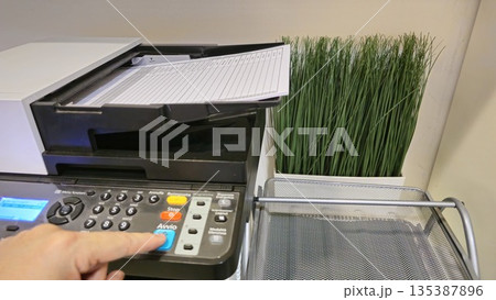 Close-Up of a Copier with Paper and Decorative Plant 135387896