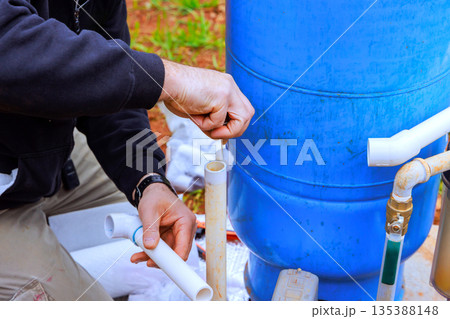 Person works on installing water pipe system near blue tank at construction site 135388148