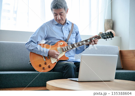 ノートパソコンでギターのオンラインレッスンを受けるシニア男性 135388604
