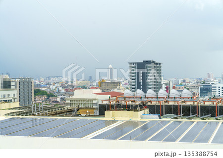 Solar panels installed on a city rooftop with industrial HVAC systems and a dense urban skyline background. Sustainable energy and modern infrastructure in a metropolitan area under a cloudy sky. Solar panels installed on a city rooftop with industrial HVAC systems and a dense urban skyline background. Sustainable energy and modern infrastructure in a metropolitan area under a cloudy sky. 135388754