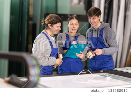 Girl and two male glazier employees with documents speaking and advising in workshop 135388912